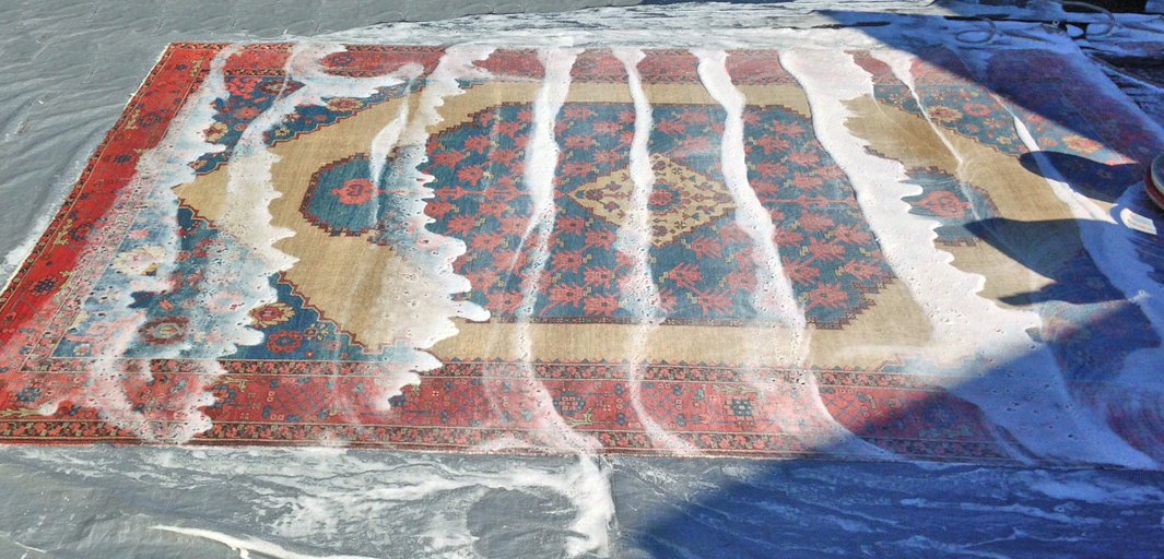 An antique Persian rug being hand washed, suds rinsing across the pile